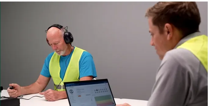 Employee wearing headphones being tested with the Soundtrace audiometer while an administrator monitors results on a laptop
